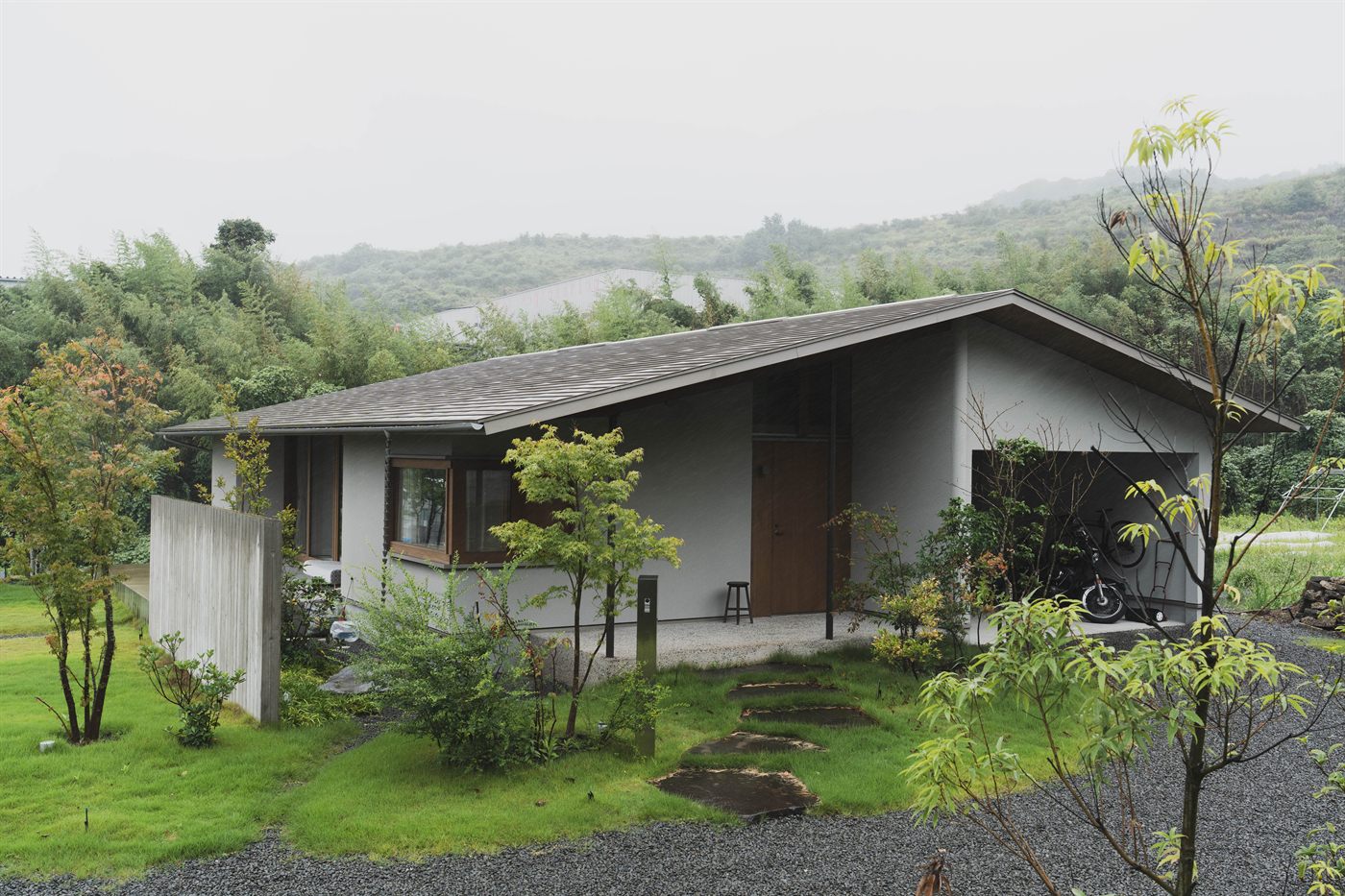 低い片流れ屋根の平屋と、飛び石のある前庭